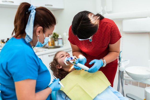 The dentist uses an ultraviolet lamp while fitting the girl with braces