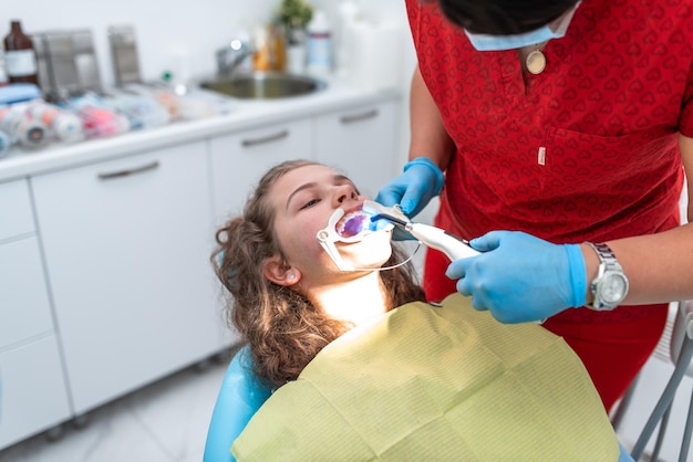 The dentist uses an ultraviolet lamp while fitting the girl with braces