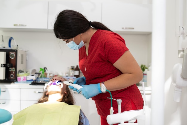 The dentist uses an ultraviolet lamp while fitting the girl with braces