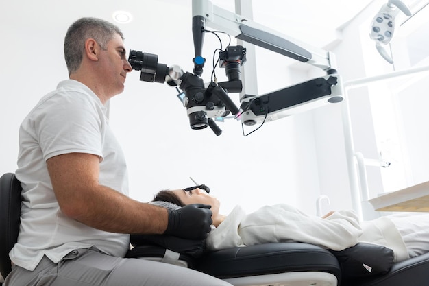 Стоматолог, использующий стоматологический микроскоп для лечения зубов пациента в стоматологической клинике, кабинете, медицине, стоматологии