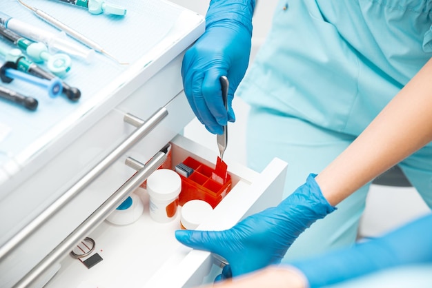 A dentist wearing disposable gloves has opened a drawer and taken some dentistry tools from it