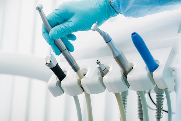 A dentist wearing gloves in the dental office holds a tool before working.