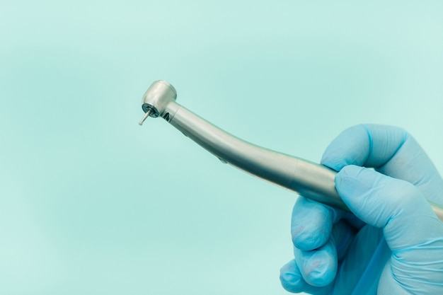 A dentist wearing gloves in the dental office holds a tool before working.