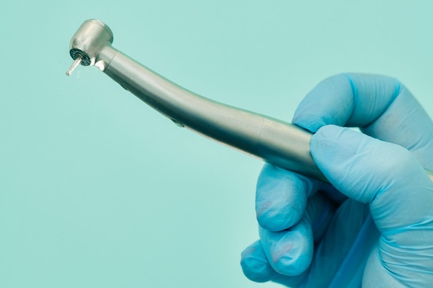 A dentist wearing gloves in the dental office holds a tool before working.