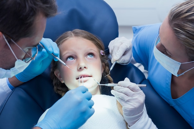 Dentist with assistant examining girls teeth