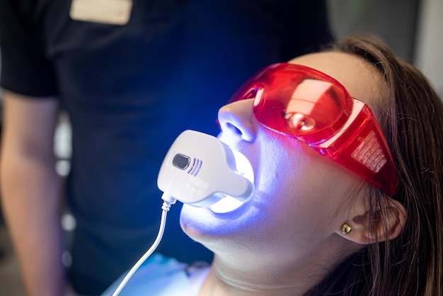 Foto il dentista con un assistente in tuta utilizza lampade uv durante il trattamento dei denti di un paziente