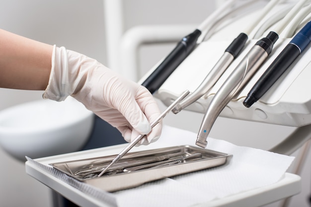 Dentist with gloved hand is picking dental equipment in dental office. Close-up