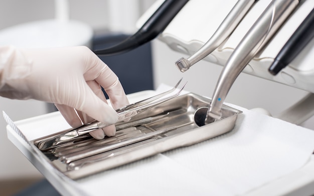 Dentist with gloved hand is picking dental tweezers in dental office