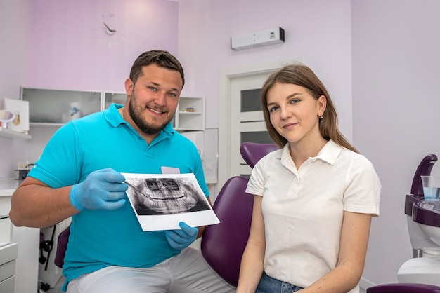 손으로 스레이 이미지를 가리키는 치과 의사가 여성 환자와 약물과 수술 치료에 대해 이야기하고 구강의 치과 건강 치료