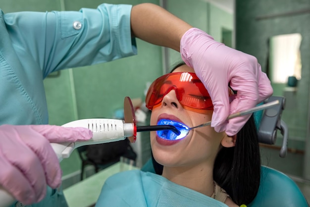 Dentist with ultraviolet lamp in dentistry making whitening to\
patient