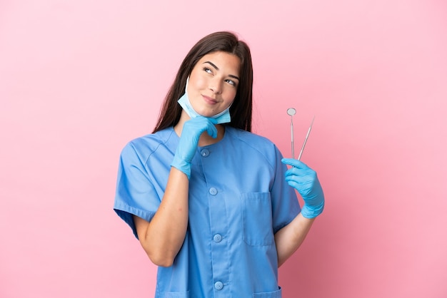 Dentist woman holding tools isolated on pink background and looking up