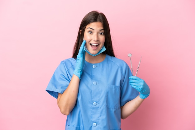 驚きとショックを受けた表情でピンクの背景に分離されたツールを保持している歯科医の女性