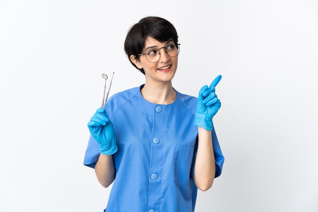 Dentist woman holding tools isolated on pink space pointing up a great idea