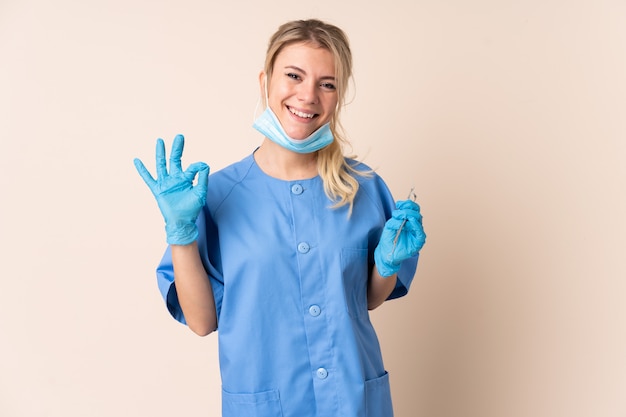 Dentist woman holding tools over isolated showing an ok sign with fingers