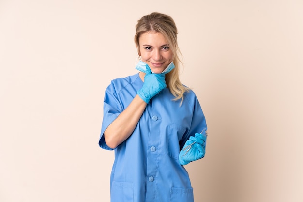 Dentist woman holding tools over isolated wall laughing