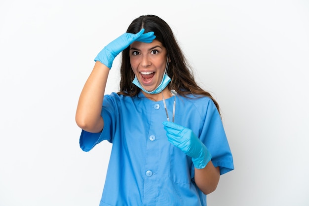 Donna dentista che tiene gli strumenti su sfondo bianco isolato facendo un gesto a sorpresa mentre guarda di lato