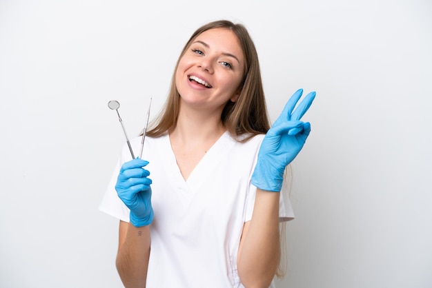 웃 고 승리 기호를 보여주는 흰색 배경에 고립 된 도구를 들고 치과 의사 여자