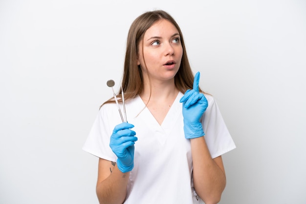 Dentist woman holding tools isolated on white background thinking an idea pointing the finger up