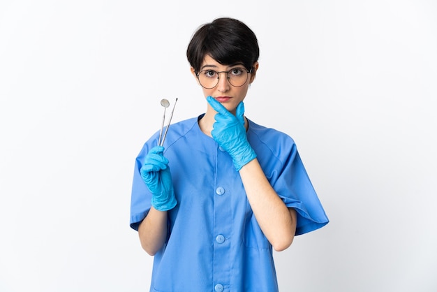 Dentist woman holding tools on pink having doubts while looking up