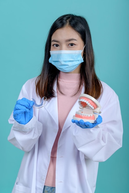 ブルースクリーンの背景に歯のモデルと歯列矯正リテーナを保持している歯科医の女性。歯科治療と健康な歯。