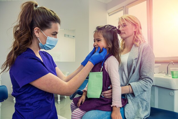 Женщина-дантист в медицинской одежде проверяет зубы девочки, чтобы избежать кариеса