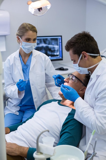 Dentists examining a male patient with tools