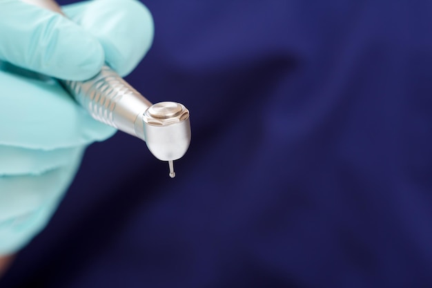 Dentists hand in a latex examination glove with a dental handpiece and a blurred blue medical gown