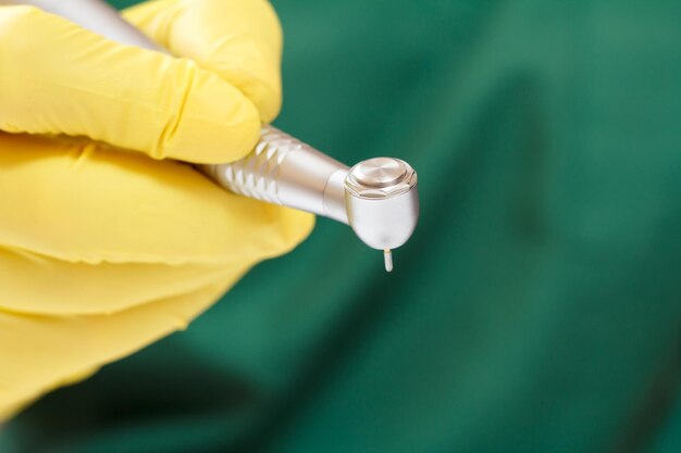 Dentists hand in a yellow latex glove with new highspeed dental handpiece on blurred background