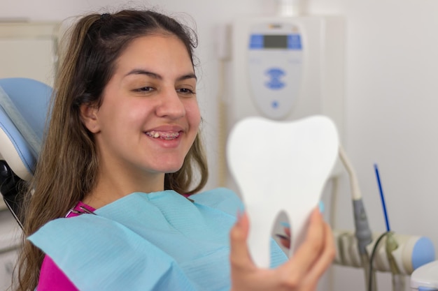 Foto all'ufficio del dentista una ragazza adolescente felice che guarda le sue apparecchiature dentali e i suoi denti allo specchio