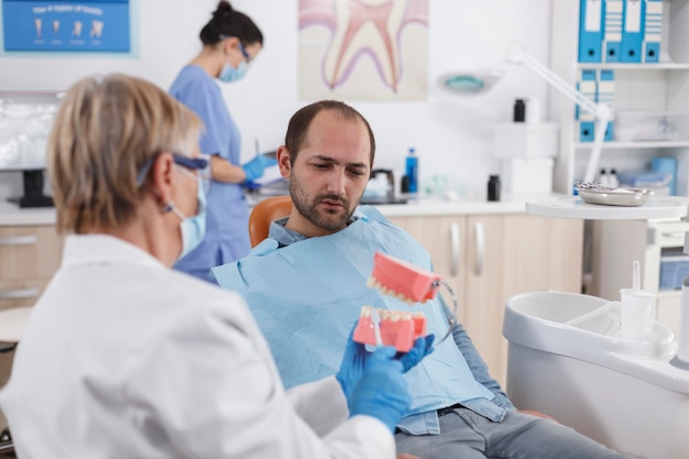 Photo dentists showing dentures to patient in clinic