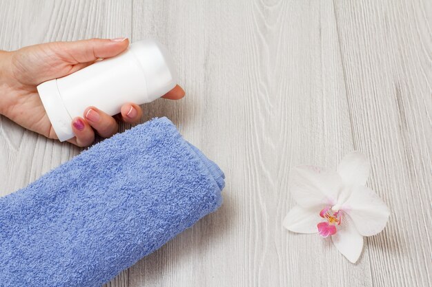 Deodorant in de hand van de vrouw, handdoek met orchidee op een grijze houten achtergrond met kopieerruimte. Vrouwen cosmetica en accessoires. Bovenaanzicht.