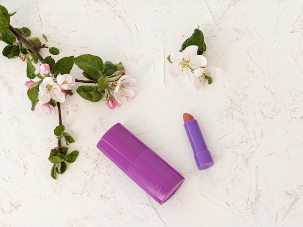 Deodorant, a lipstick, tulip and flowers of an apple tree on the structured background. Women's accessories for bath procedures. Top view.