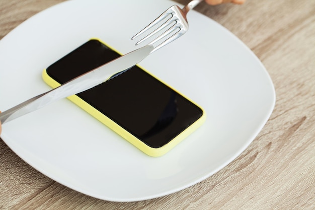 Dependence on the phone, close up a woman's hands holding a fork and a knife over the phone on plate.