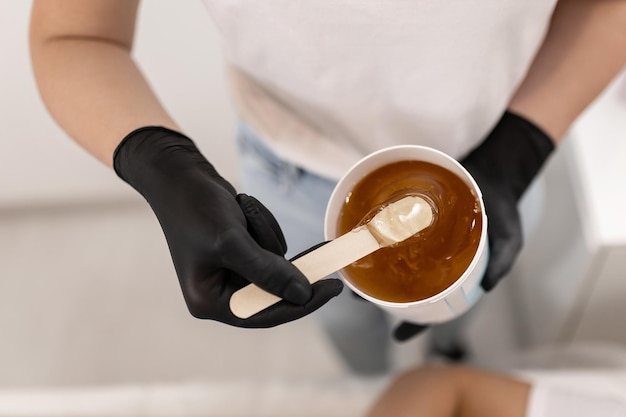 Depilation master picks sugar honey wax for epilation from a jar with a wooden spatula
