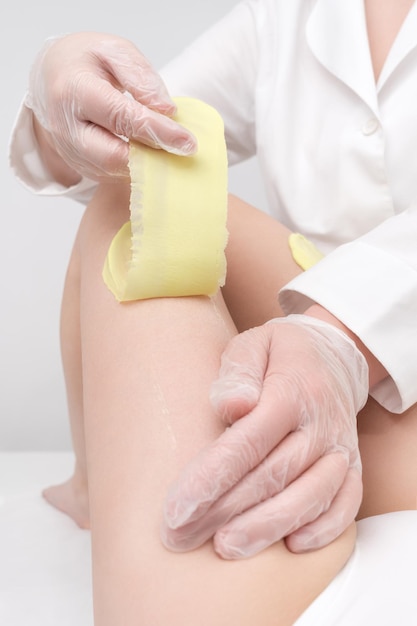 Photo depilation procedure cosmetologist hands in gloves removing hair on women leg waxing process