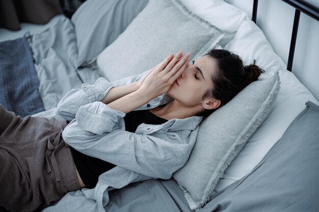 Photo depressed brunette woman suffering from emotional pain while lying on bed at home