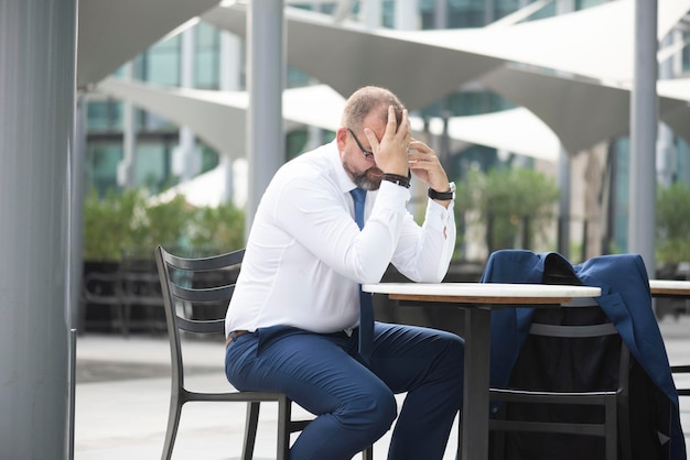 Foto uomo d'affari depresso che parla al cellulare mentre è seduto su una sedia all'aperto