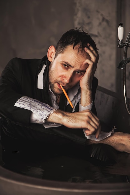 Depressed crazy man writer mental health in bathtub in bathroom at home