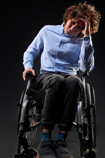 Depressed disabled man has no meaning in life, he sits on wheelchair, unhappy with something, sits looking down. isolated on black background