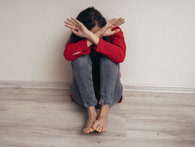 Depressed girl in a red shirt against the wall