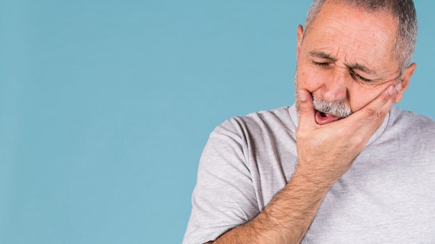 Foto uomo malato depresso che ha mal di denti e che tocca la sua guancia sul contesto blu