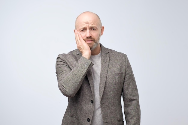 Depressed ill mature man having terrible toothache and touching cheek