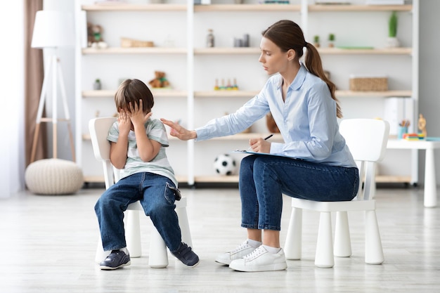 Depressed little boy crying during psychological session with professional therapist caring woman