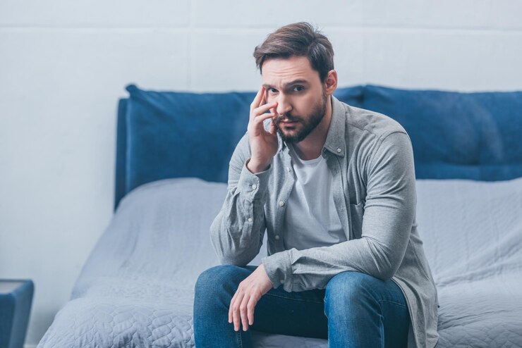 Photo depressed man sitting on bed looking at camera and grieving at home