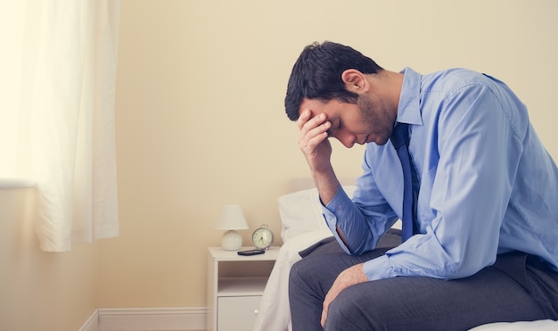 Depressed man sitting head in hands on his bed