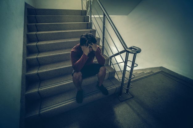 Photo depressed man sitting head in hands on the staircase in the fire escape or building