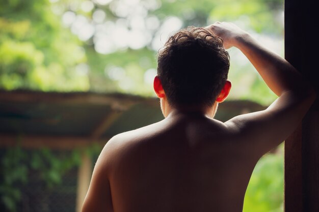 Depressed man standing beside windows and thinking