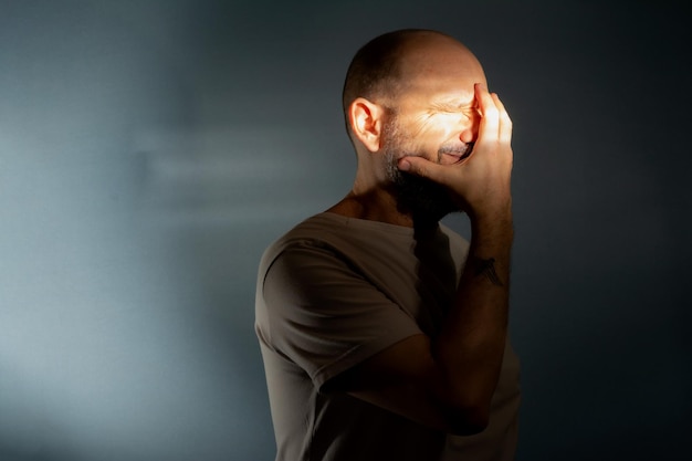 Депрессивный мужчина средних лет с рукой на лице, изолированный на сером фоне, имеющий финансовые проблемы или страдающий от одиночества
