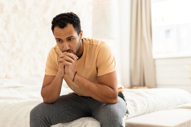 Depressed middle eastern man sitting thinking in modern bedroom