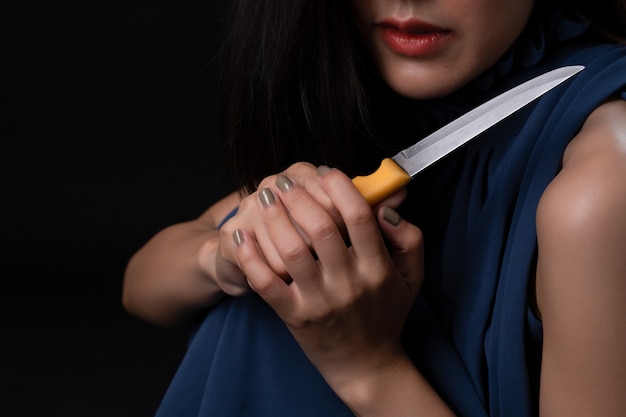 Depressed sad young female holding knife in hand on dark.